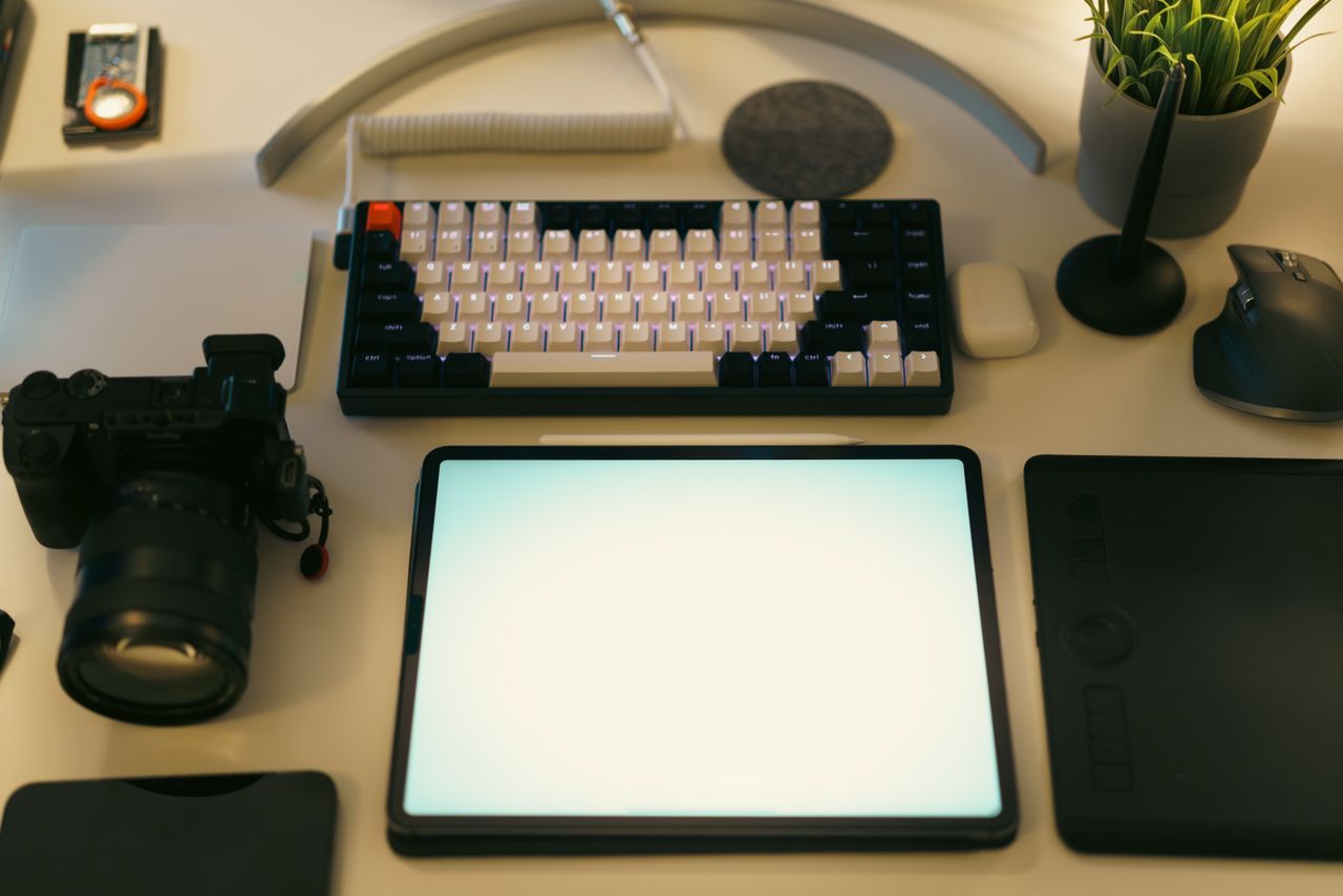 gallery-03 A sleek desk arrangement with a digital tablet, keyboard, camera, and plant, well suited for creative work.